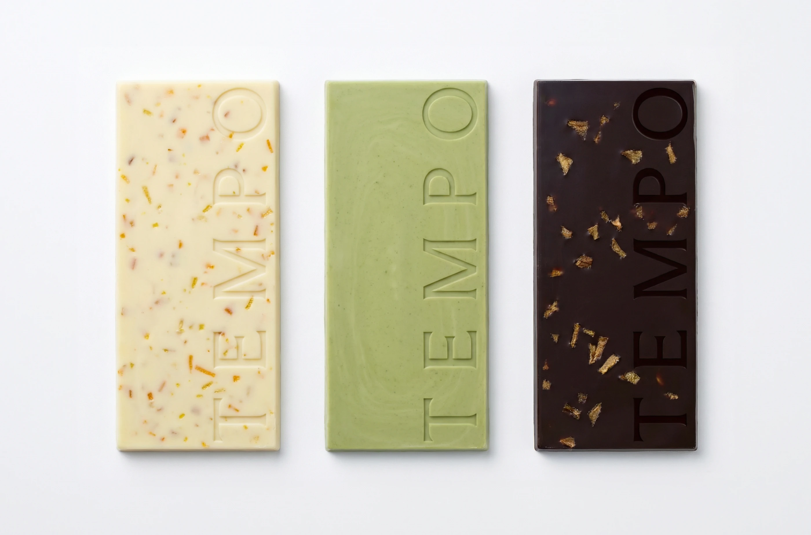 Three TEMPO chocolate bars by LYM Design Studio shown without packaging, featuring white chocolate with inclusions, green matcha chocolate, and dark chocolate with gold flakes and embossed typography.
