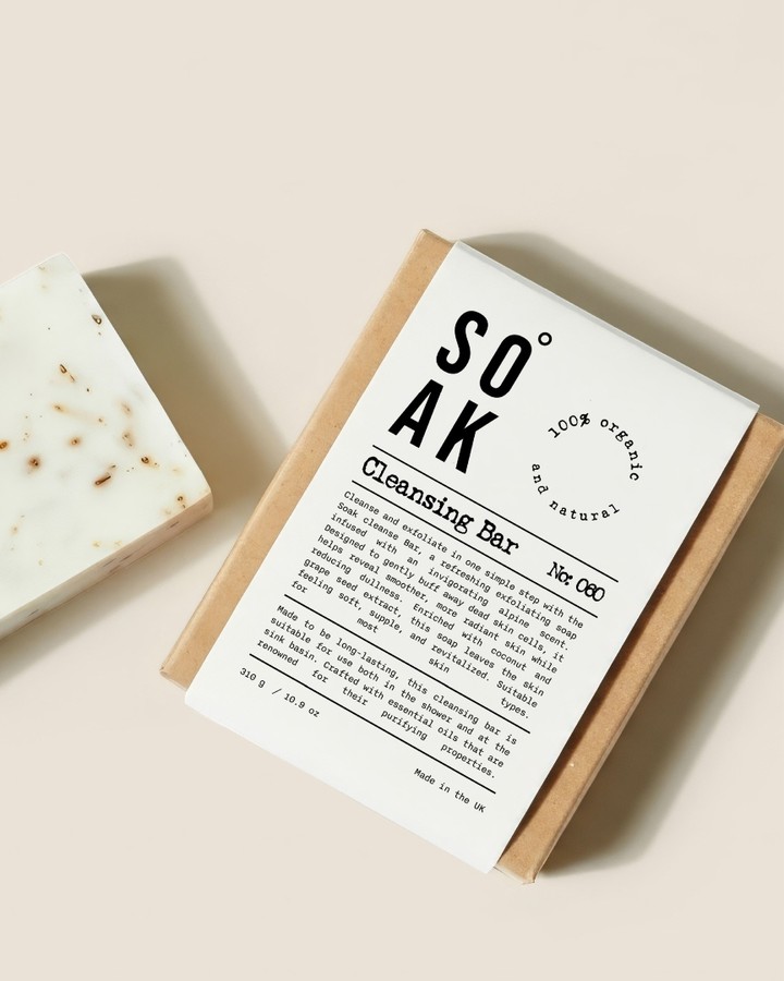 Soak Cleansing Bar packaging with black minimalist typography shown beside a textured soap bar on a soft neutral background.