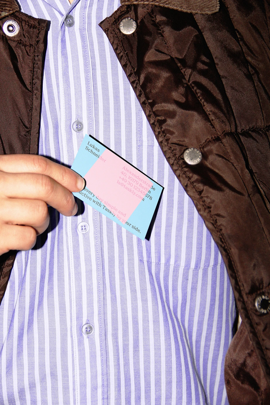 A person pulling a pastel blue and pink Taskly business card from their jacket pocket, highlighting the brand identity’s bold color blocking and modern typography in a real-world lifestyle context.