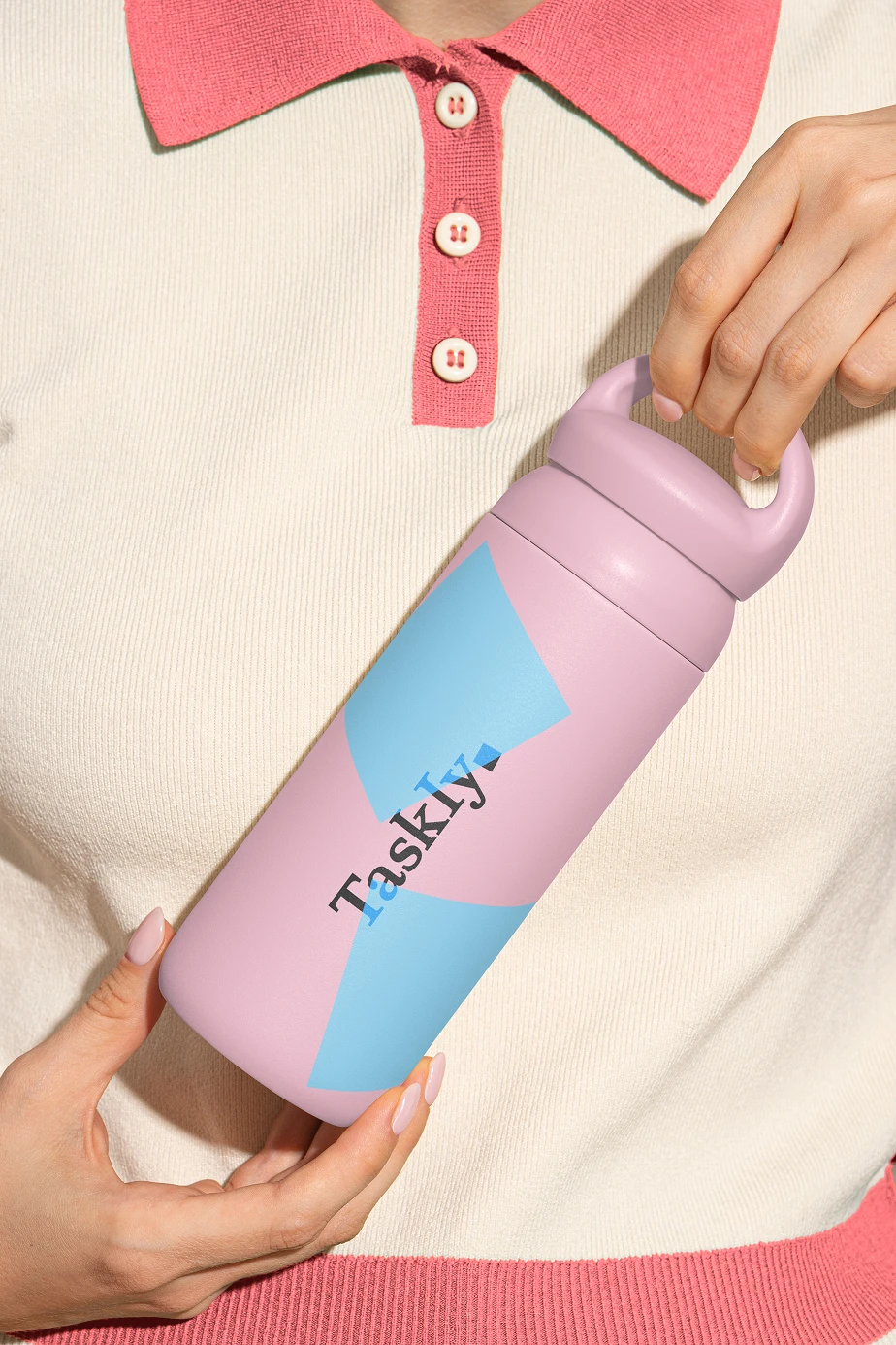 A hand holding a pastel pink and blue Taskly water bottle decorated with bold geometric color blocking and the brand’s playful typography, emphasizing the versatility of the identity system across lifestyle products.