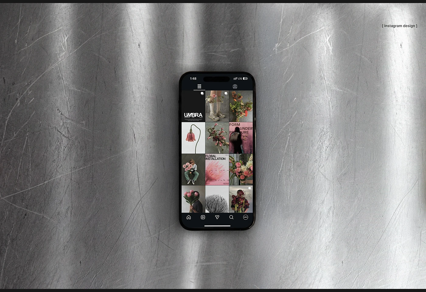 UMBRA Instagram design mockup shown on a phone over a scratched metallic surface, featuring a grid of floral photography, brand typography, and dark editorial social media layouts.