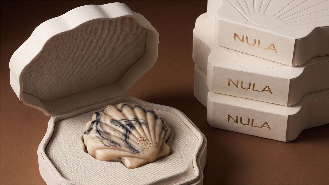 NULA packaging design featuring a marbled shell-shaped soap presented inside a sculptural cream box with gold foil branding.