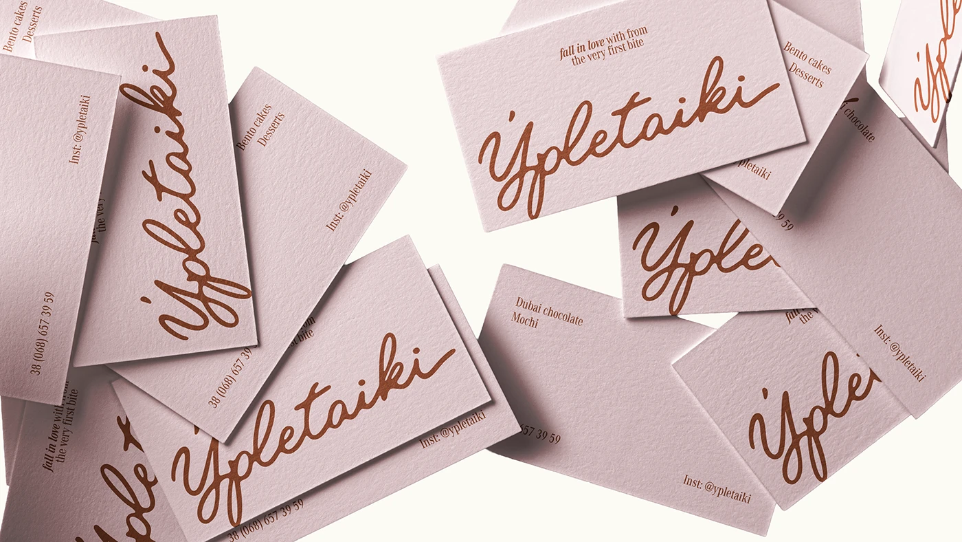 Textured blush pink Ypletaiki business cards featuring brown handwritten script logo and refined café brand identity typography.