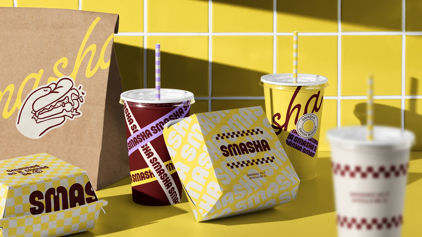 Product lineup of Smasha cups, burger boxes, and takeaway packaging featuring yellow, burgundy, and checkered patterns arranged against a tiled yellow background.
