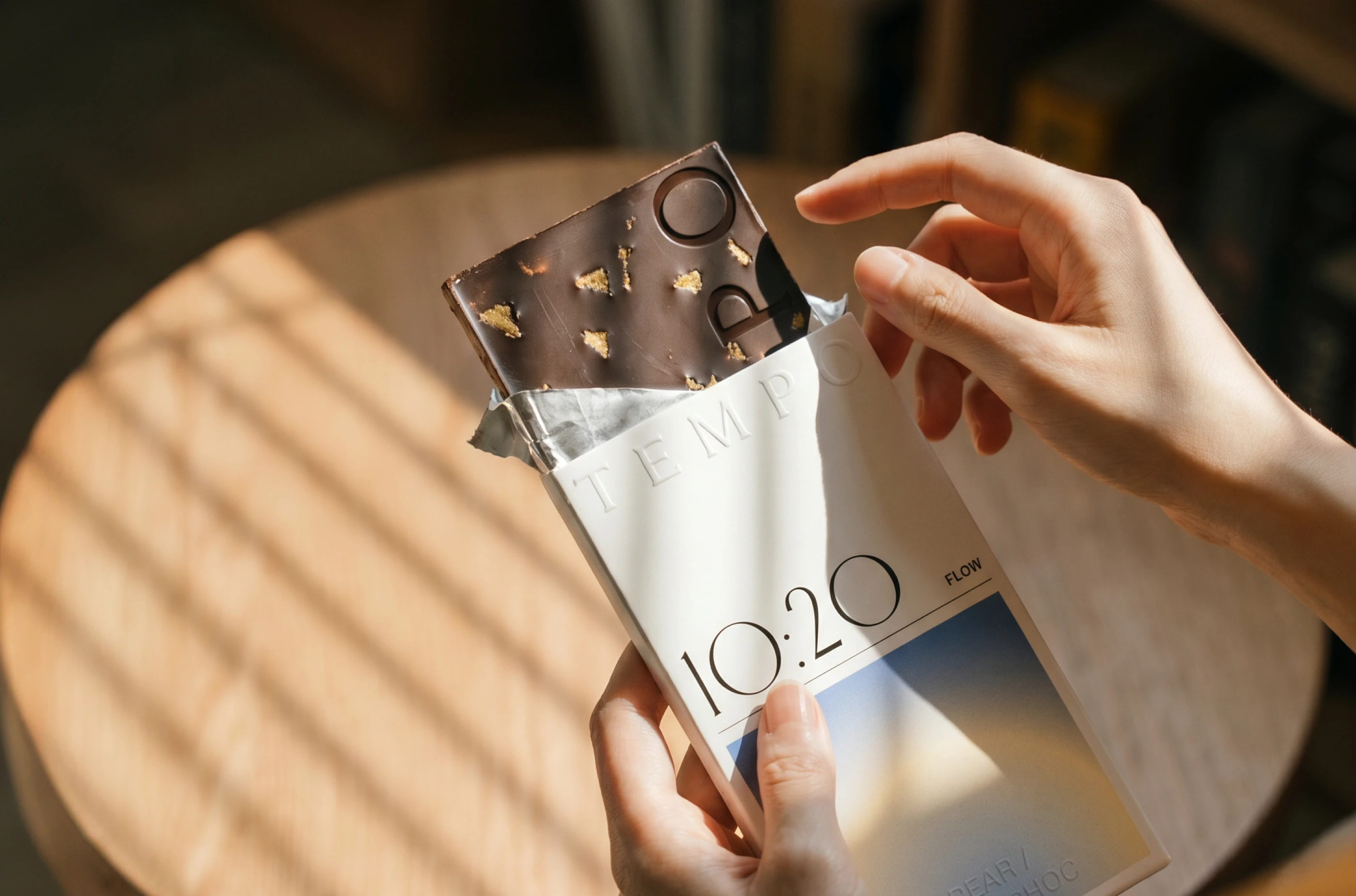 TEMPO chocolate packaging design by LYM Design Studio showing a dark chocolate bar with gold flakes being pulled from a white wrapper labeled 10:20 Flow.