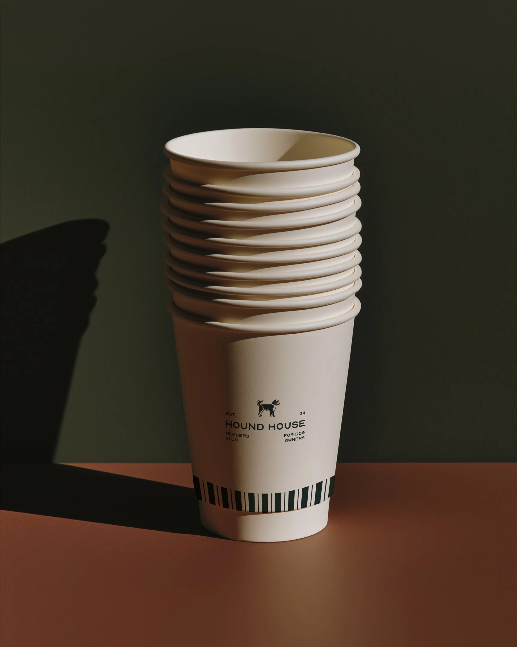 Stack of branded takeaway cups featuring the Hound House logo and striped detailing, representing café and beverage branding within a pet hospitality brand identity.