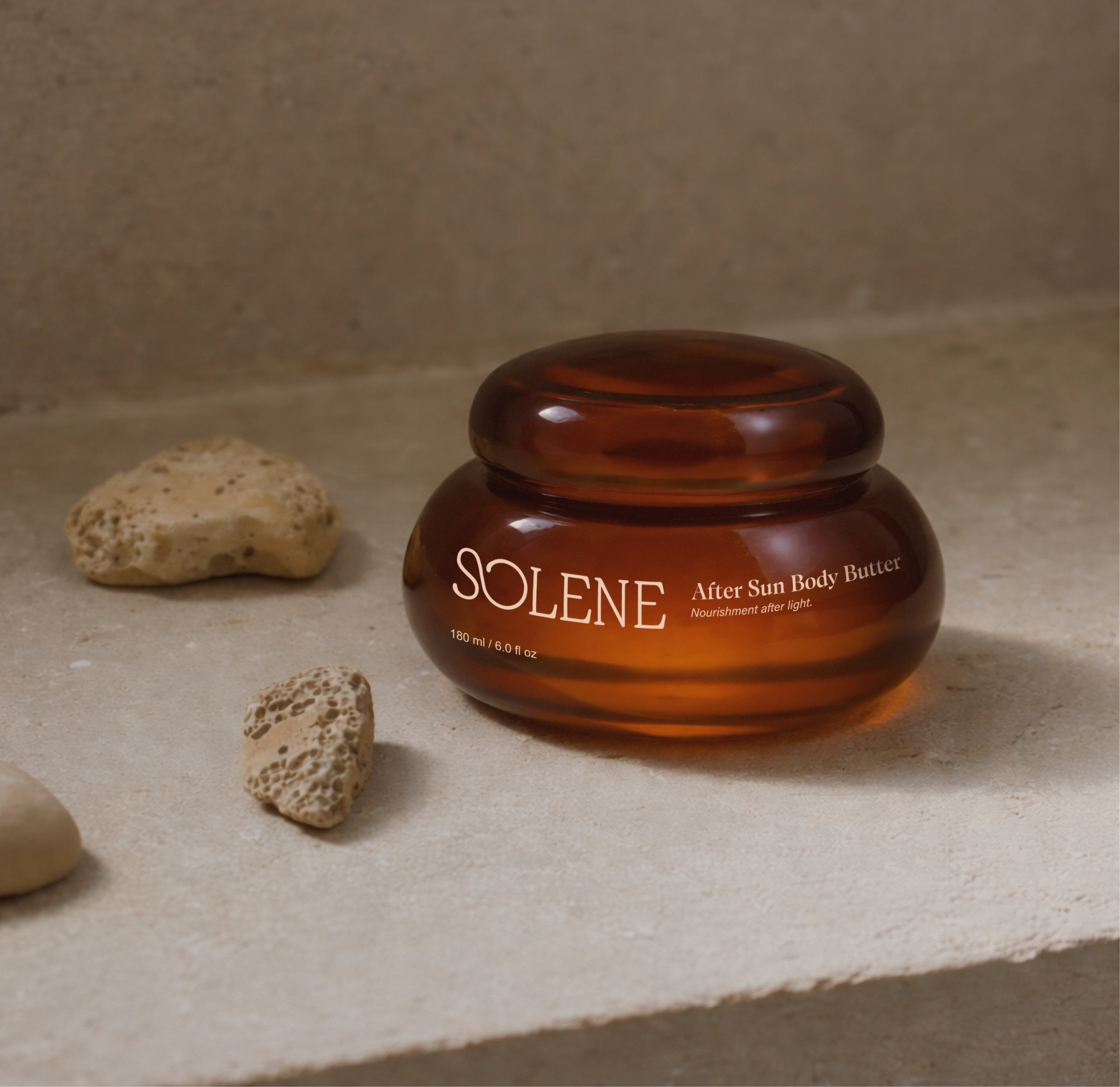 Solene SPF after sun body butter in a rounded amber jar on a stone surface with natural rocks, showing the warm skincare packaging and refined body care identity.