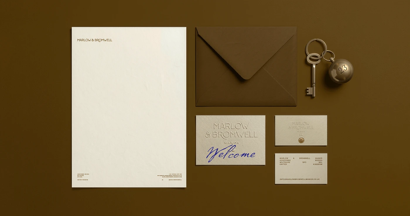 Marlow & Bromwell Manor stationery suite including letterhead, brown envelope, welcome card with blue script, business cards, and vintage key fob arranged on olive background