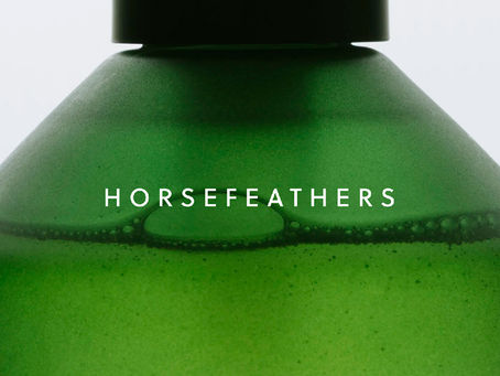 Close-up of a green Horsefeathers skincare bottle with white wordmark typography across the glass, showing the brand’s minimalist bath and body packaging design by Studio Andor.