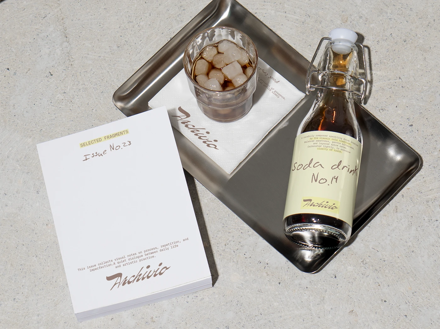 Archivio Coffee Cultura soda bottle labeled “Soda drink No.14” styled with iced coffee, metal tray, and printed “Selected Fragments” booklet referencing archival concept.