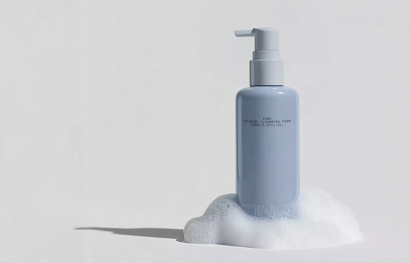 Single soft blue ZING cleansing foam bottle standing in white foam, featuring minimal black typography and subtle embossed branding on a clean white background.