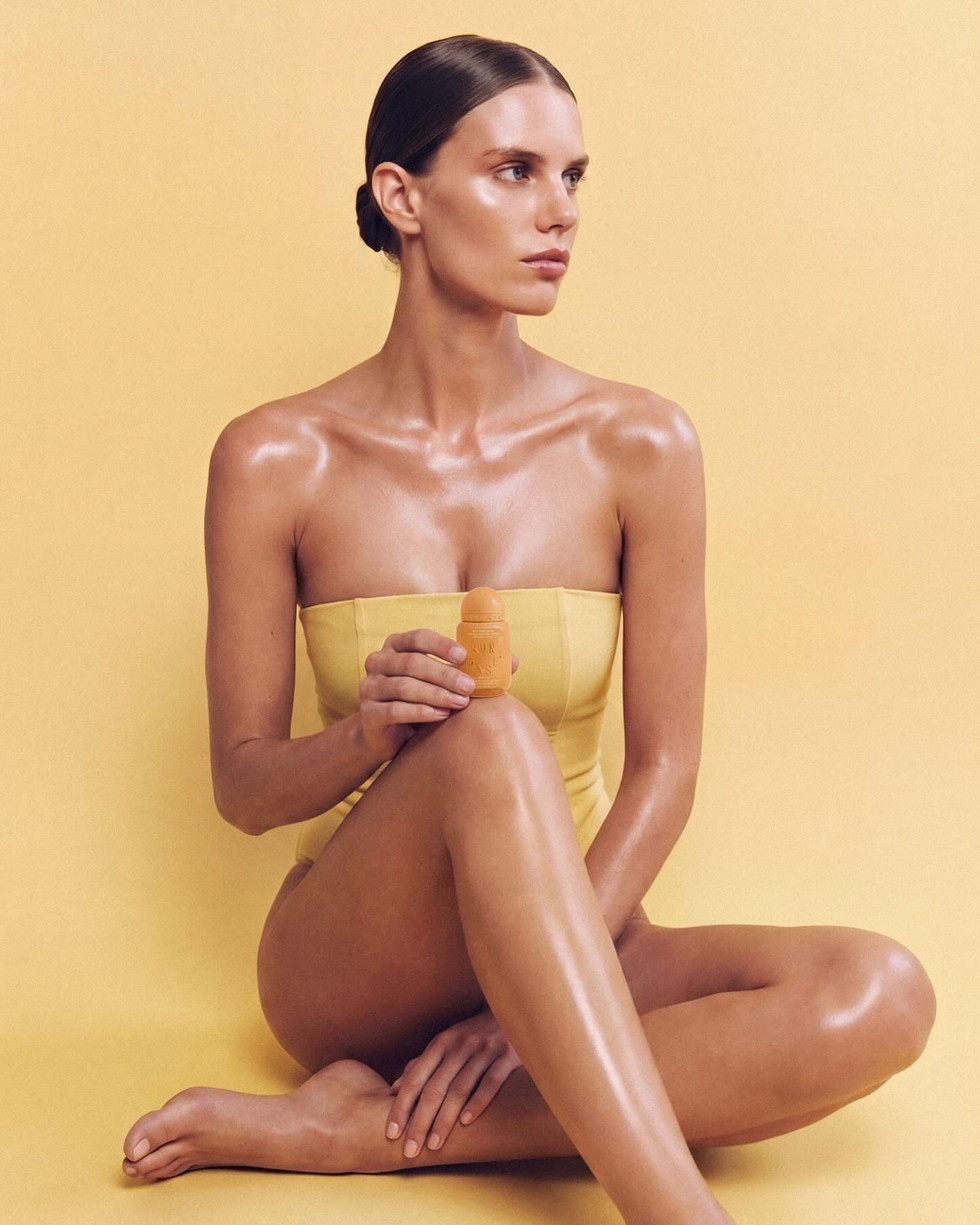 Model holding Sunbase sunscreen bottle against warm yellow backdrop, lifestyle skincare campaign with minimalist brand aesthetic