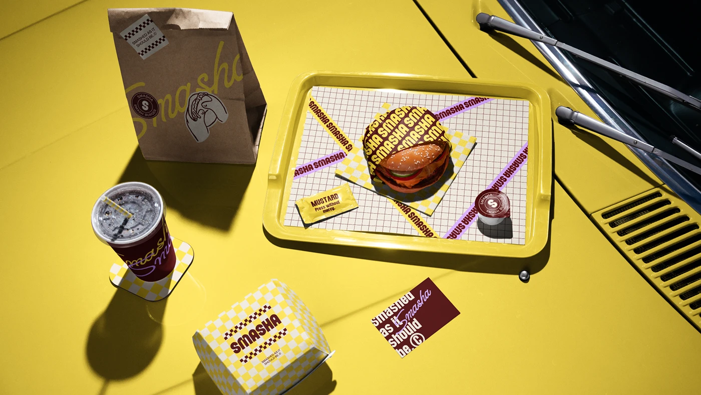 Overhead view of a Smasha meal set on a yellow car hood, featuring a burger in branded packaging, drinks, tray liner, and takeaway bag styled for lifestyle brand photography.