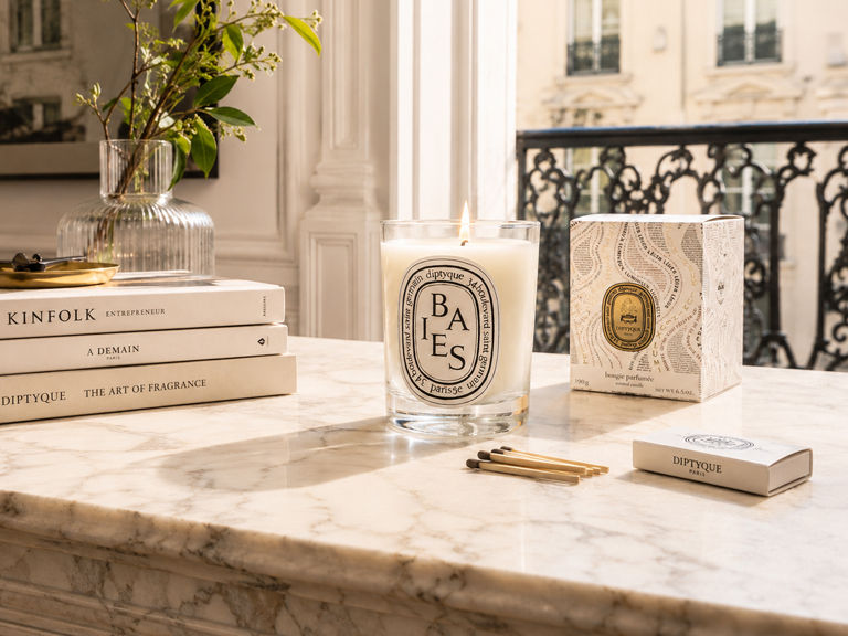 Diptyque candle and packaging styled on a marble surface with books, matches, and soft natural light, illustrating luxury product branding and hero product storytelling.