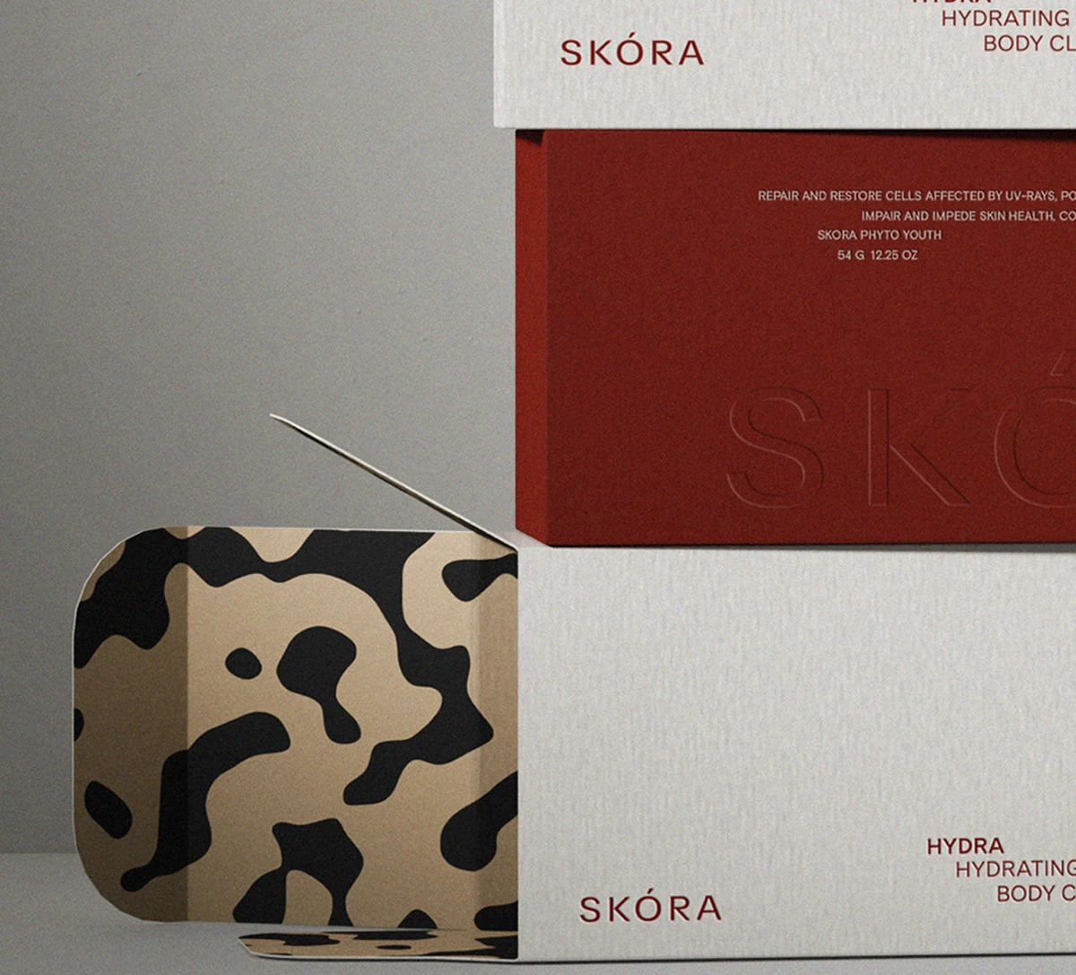 Close-up of Skora bodycare packaging highlighting embossed typography, astaxanthin-red panels, patterned material accents, and refined print details within the brand’s minimalist skincare identity system.