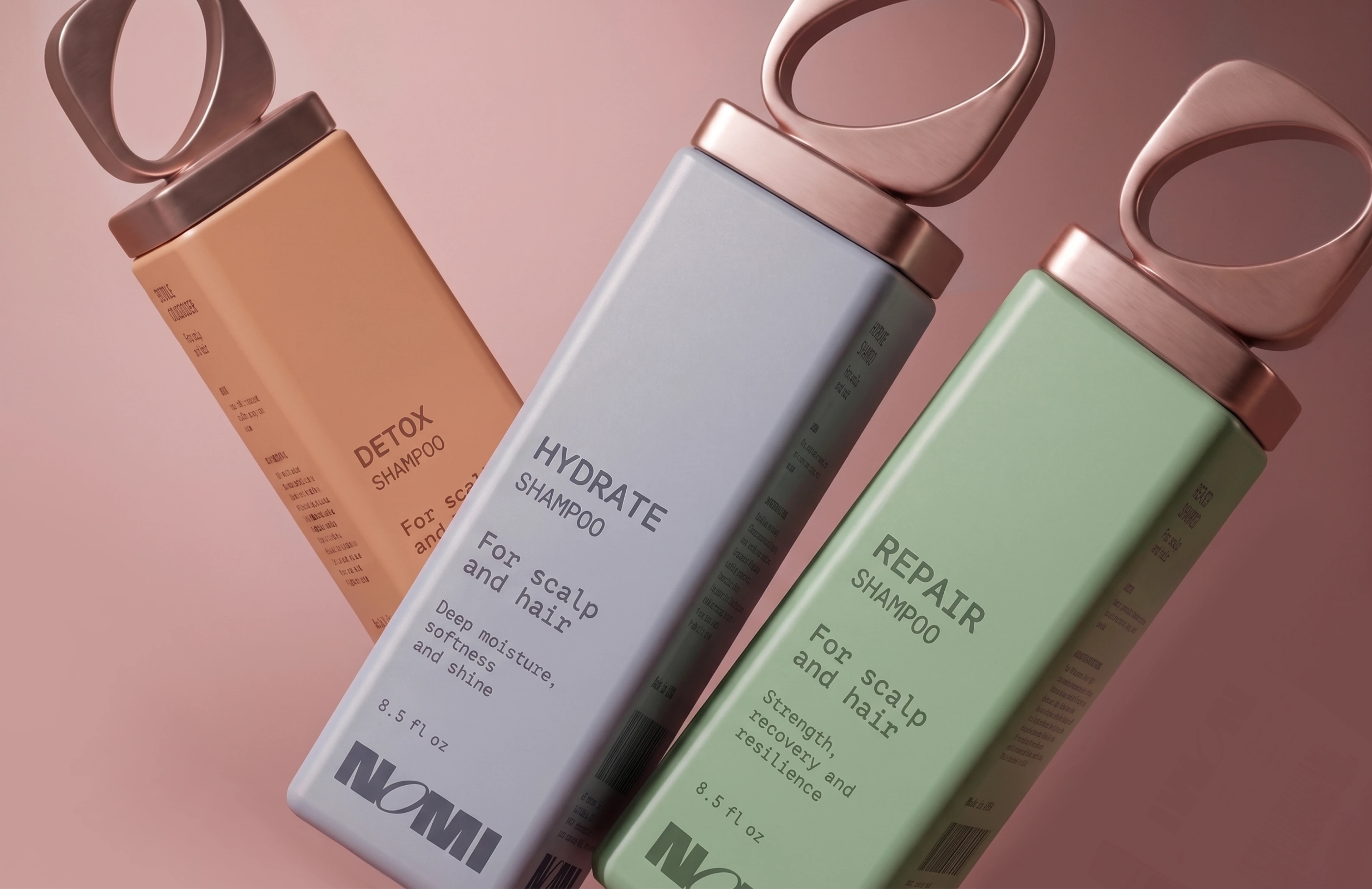 NOMI Detox, Hydrate, and Repair shampoo bottles angled across a blush background with rose-gold loop caps.