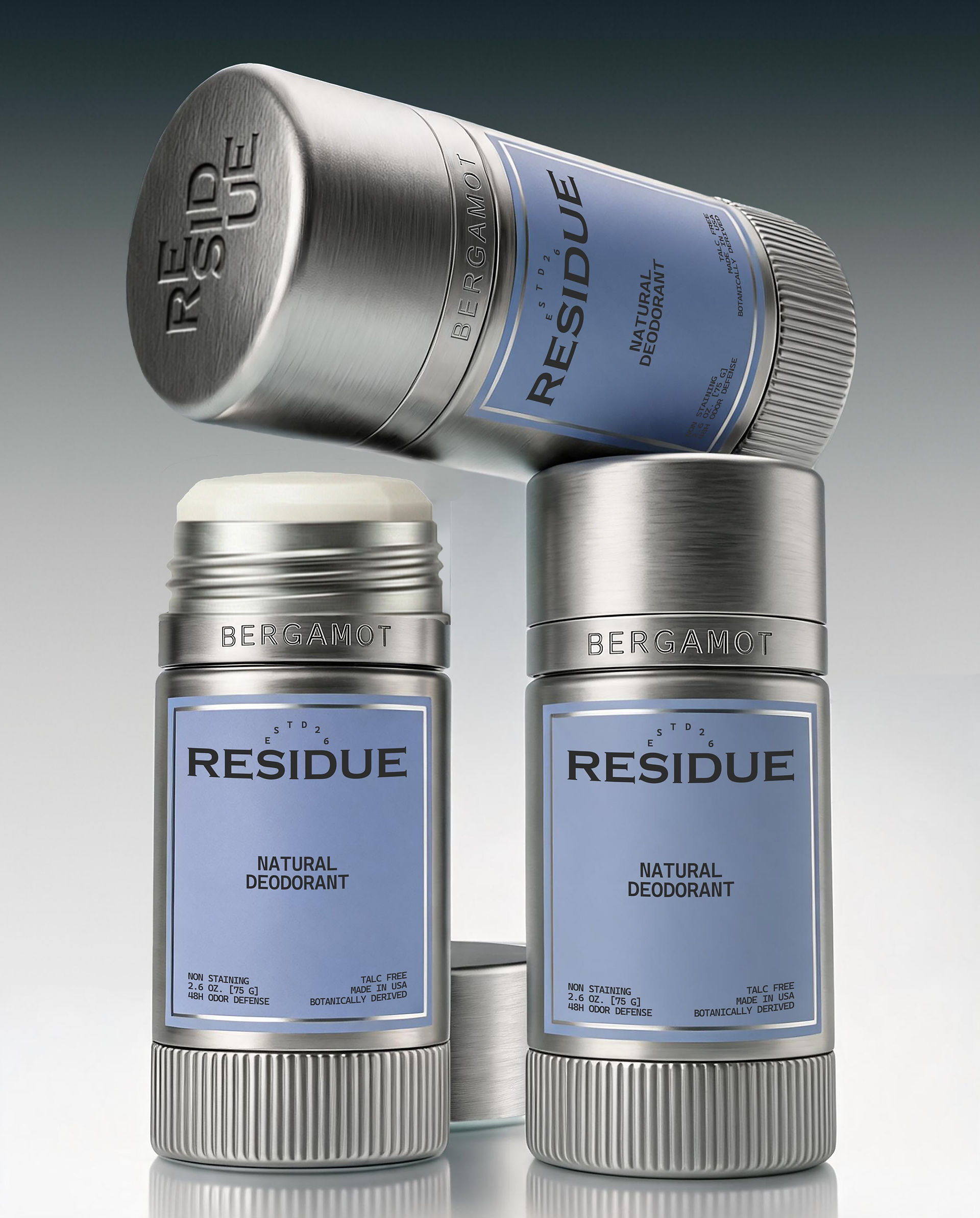 Three silver natural deodorant sticks stacked in a balanced arrangement, featuring brushed metal packaging, powder blue labels, and engraved fragrance names.