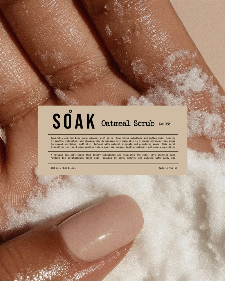 Soak Oatmeal Scrub label shown over a close-up of wet hands holding a white textured body scrub.