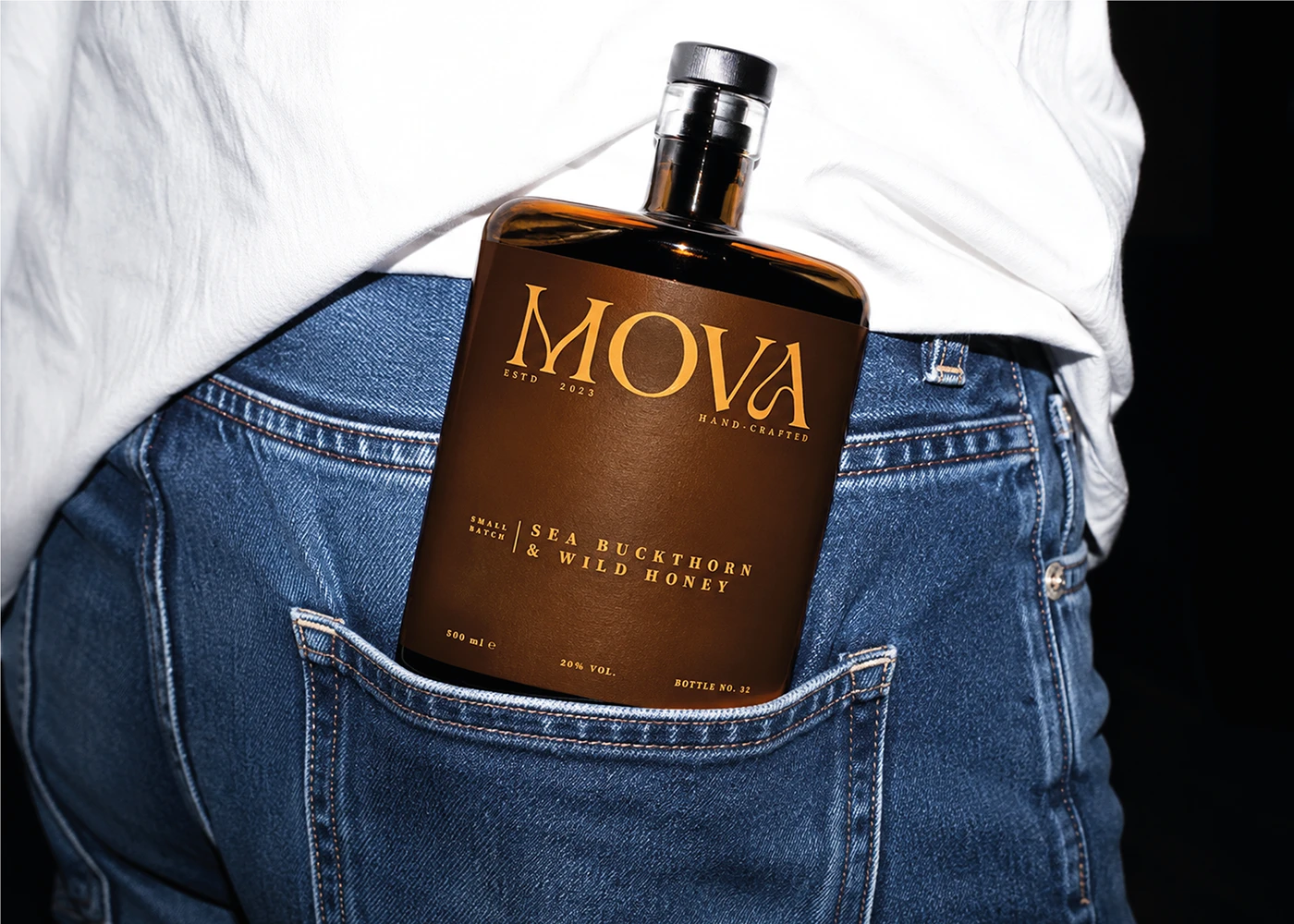 MOVA sea buckthorn and wild honey liqueur bottle with brown packaging tucked into a denim pocket.