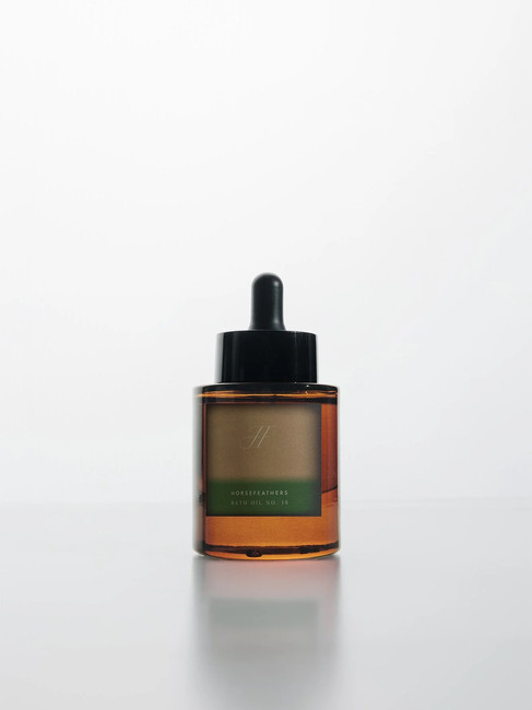 Amber Horsefeathers Bath Oil No. 15 dropper bottle with a soft green gradient label, photographed on a reflective white surface with minimal skincare packaging styling.