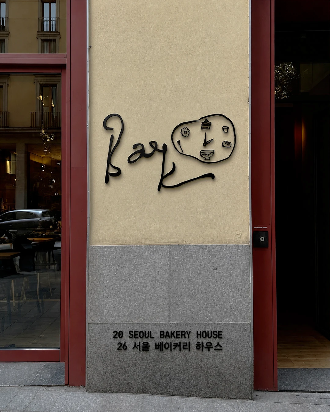 Baek Korean Bakery exterior signage mockup featuring a black handwritten logo mounted on a cream storefront wall with red architectural framing and Korean text below.