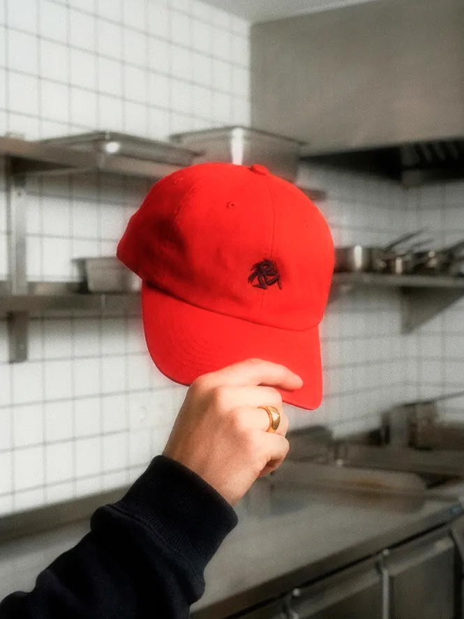 Churros Churros merchandise detail featuring a red branded cap held in a tiled kitchen environment.