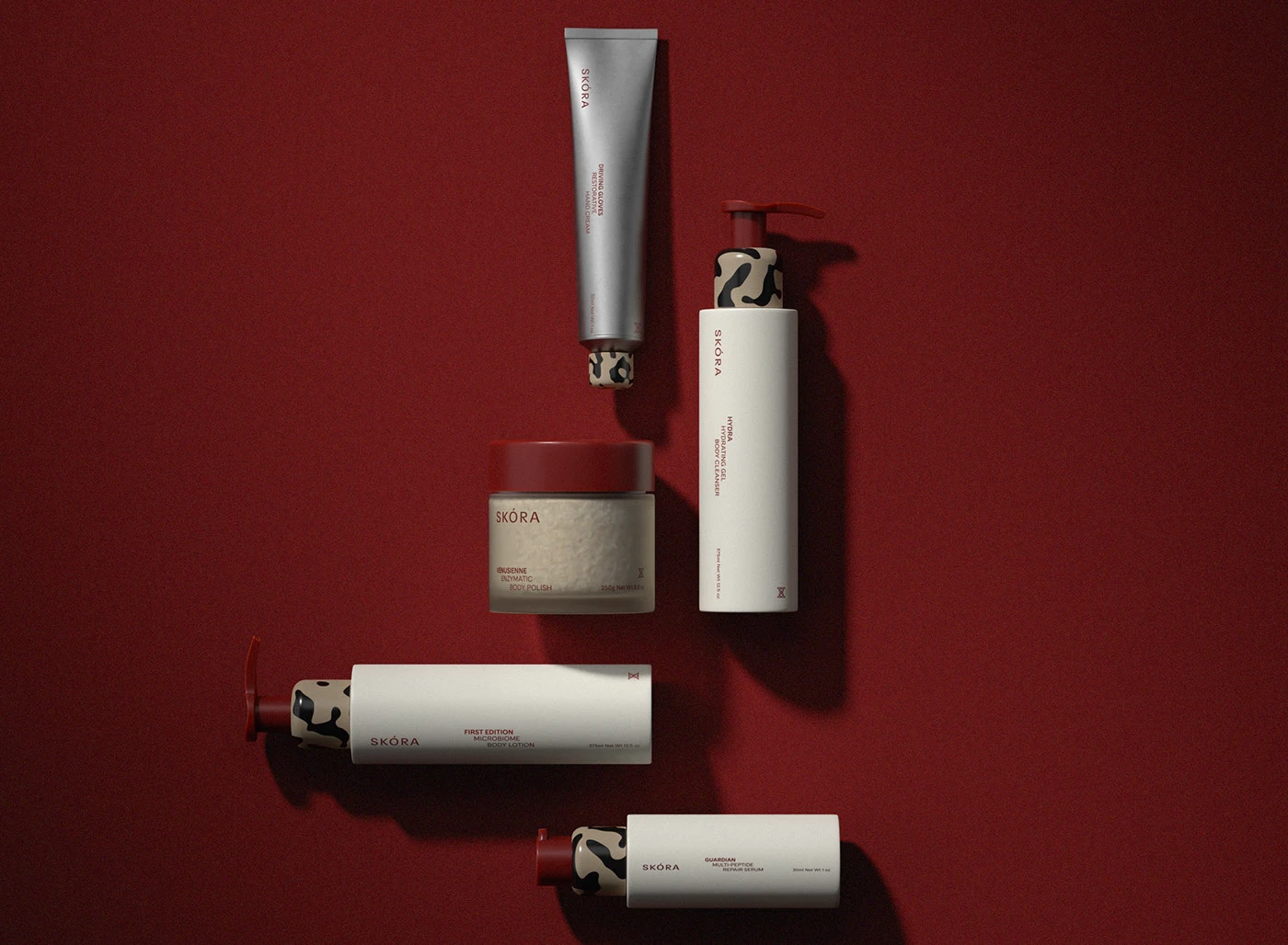 Skora bodycare packaging arranged in a flat lay on a deep astaxanthin-red background, featuring bottles, tubes, and jars with minimalist typography, sculptural caps, and refined material contrast.