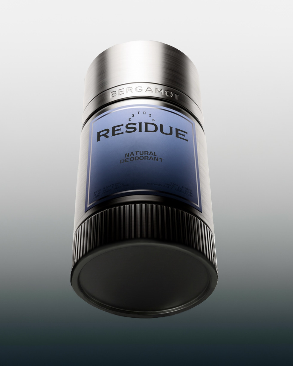 Natural deodorant stick viewed from a dramatic low angle, showing a brushed silver cap, blue label, and ribbed black base against a soft gray background.
