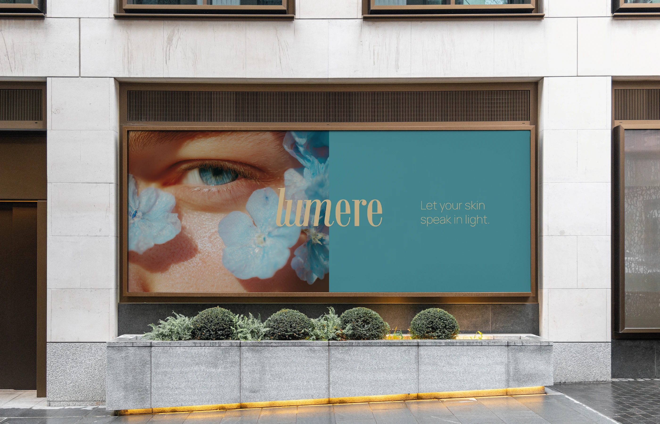 Large-scale horizontal billboard mockup on a modern stone building. The left side features a close-up of a blue-eyed model surrounded by light blue hydrangeas; the right side is a solid teal block with the gold serif 'lumere' logo and the tagline 'Let your skin speak in light.