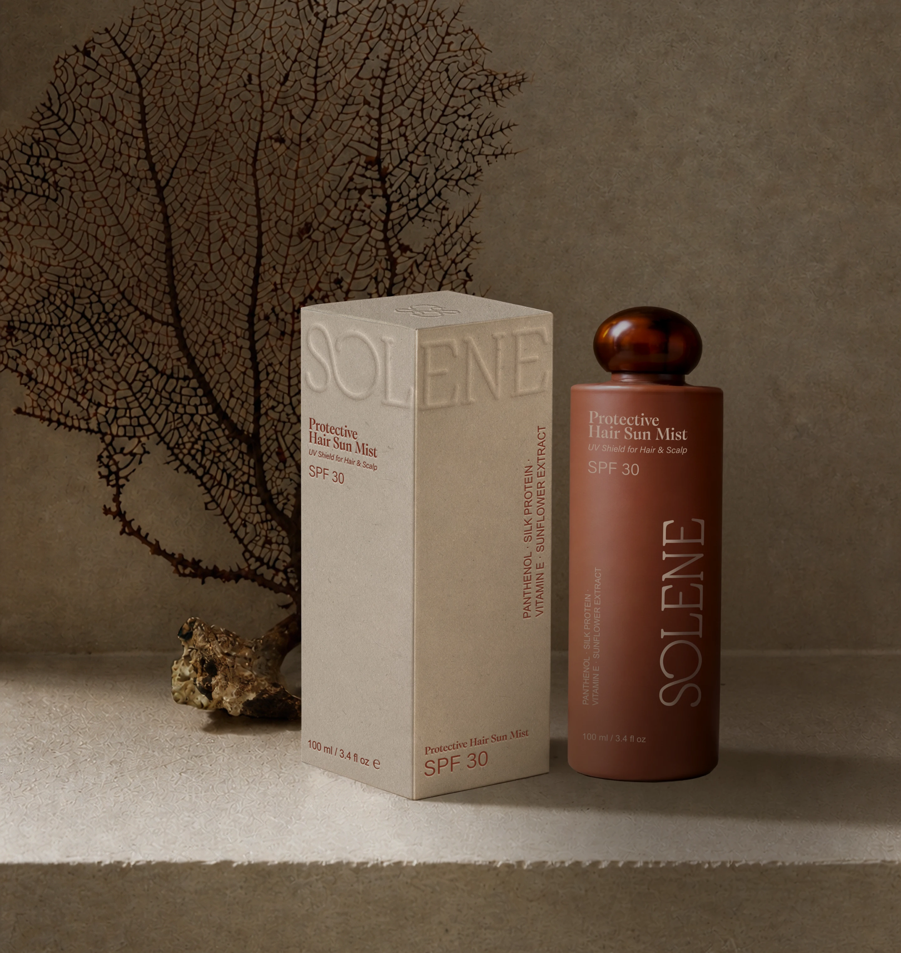 Solene SPF protective hair sun mist packaging beside a textured ivory box with blind embossed logo details, amber cap, and sea fan coral texture in the background.