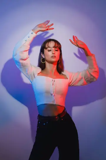 young woman standing with arms above her head in contrast pink and blue lighting