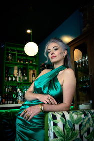 woman in bar, wearing silky green cocktail dress leaning on booth wearing lelamooi jewelry