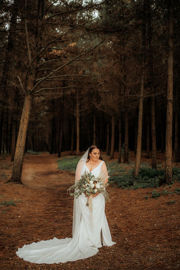 bride standing in woods forrest holding bouquet and wearing a long veil
