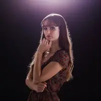 young woman with long hair standing with arm under chin and overlit