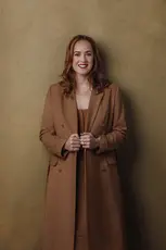 Model wearing brown coat and dress in front of brown wall