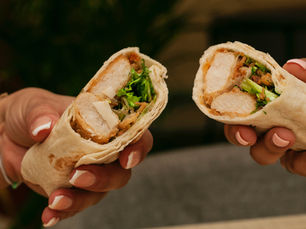 Wrap coupé en deux garni de poulet pané, salade verte, copeaux de parmesan et sauce, présenté sur une planche en bois.
