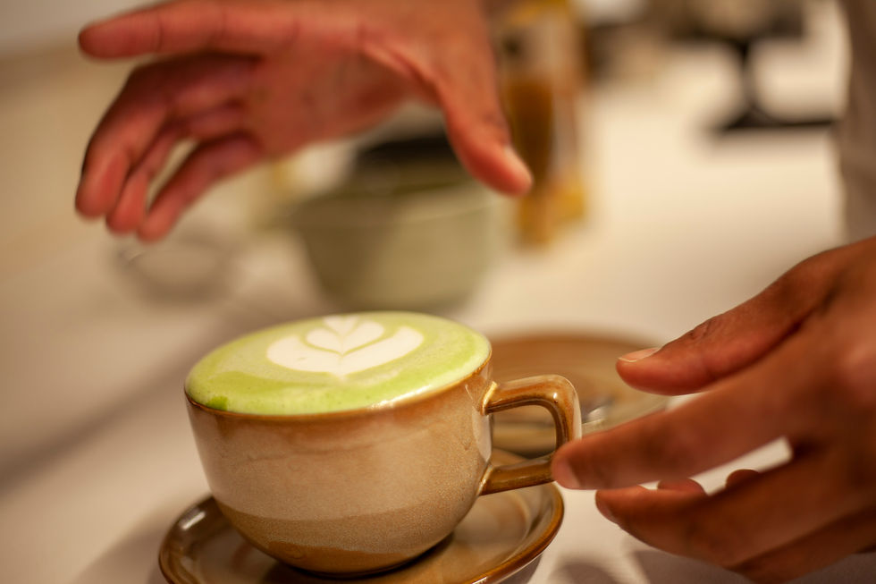 Tasse de matcha latte avec mousse et latte art, posée sur une soucoupe, avec des mains en train de la saisir.