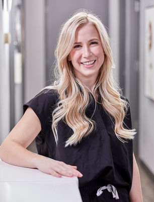 Blonde woman in dark scrubs posing against a medical office desk. By Jeff B Photography.