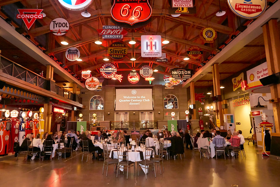 People dining at the Quarter Century Club event in a retro-themed venue, surrounded by vintage signs and gas pumps. Warm and lively ambiance. By Jeff B Photography