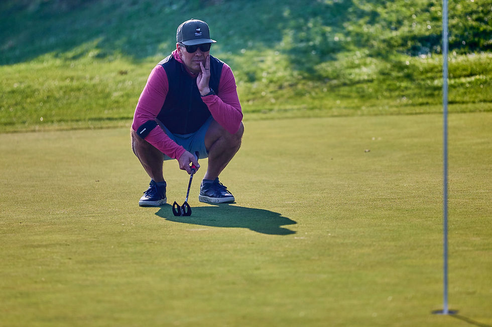 A man at a corporate golf tournament squatting down and watching a friend putt to the hole.