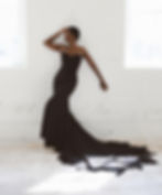 Elegant woman in black strapless mermaid gown posing against white brick wall.