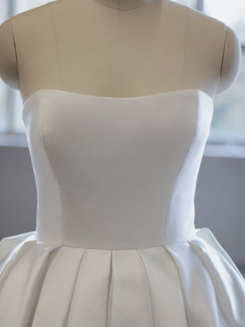 Elegant white strapless satin dress bodice on mannequin with pleats.