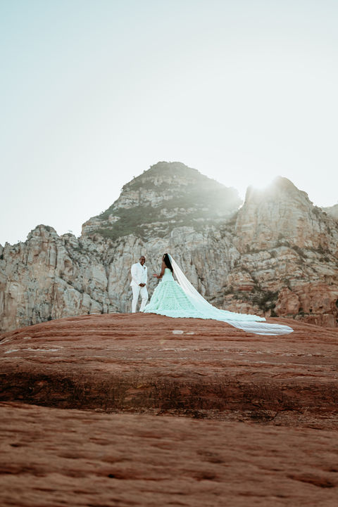 Wedding couple on rocky mountain peak with bright sun.