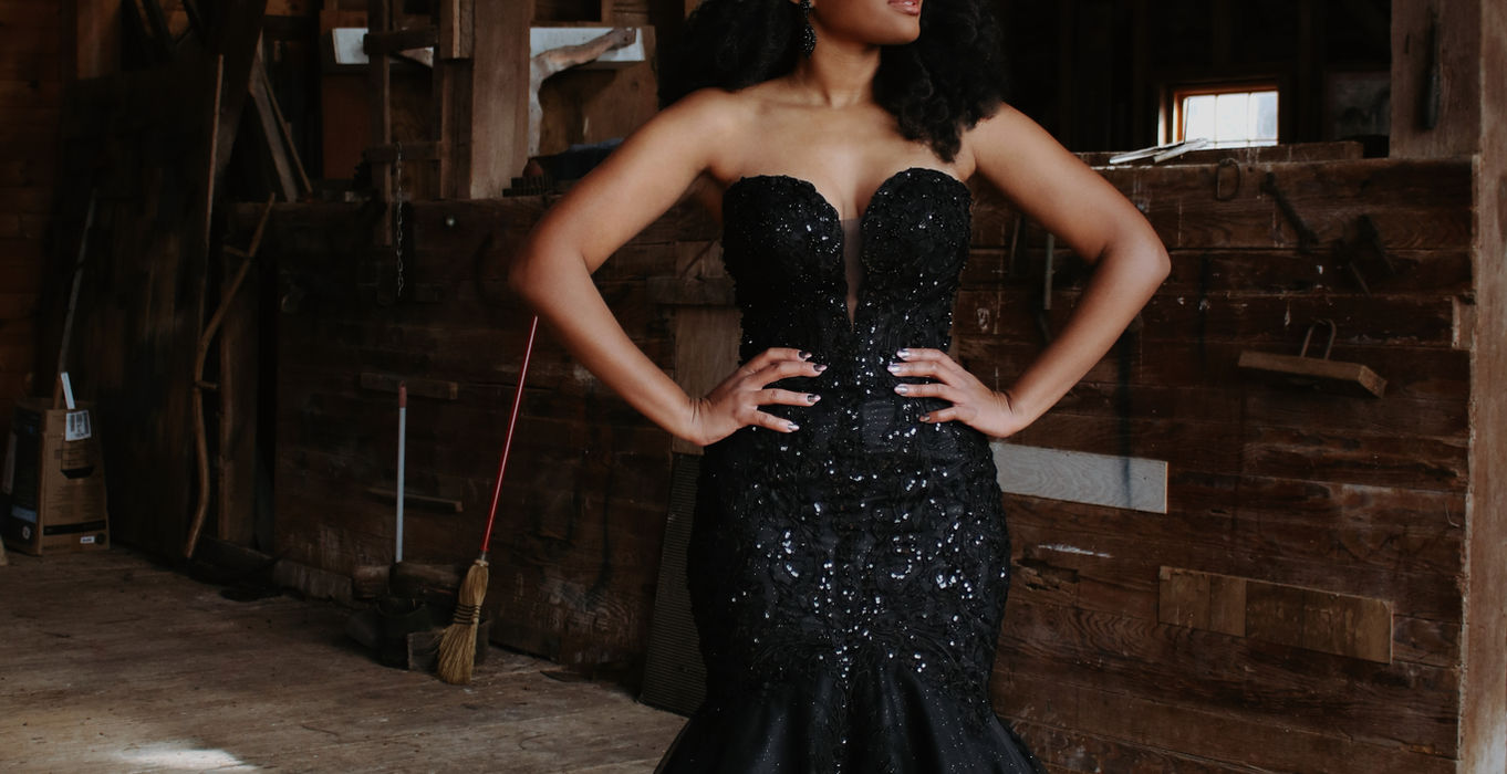 Woman in elegant black mermaid gown inside rustic wooden barn.