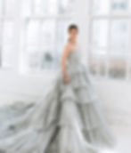 Woman in stunning gray ruffled tiered ballgown by large windows.