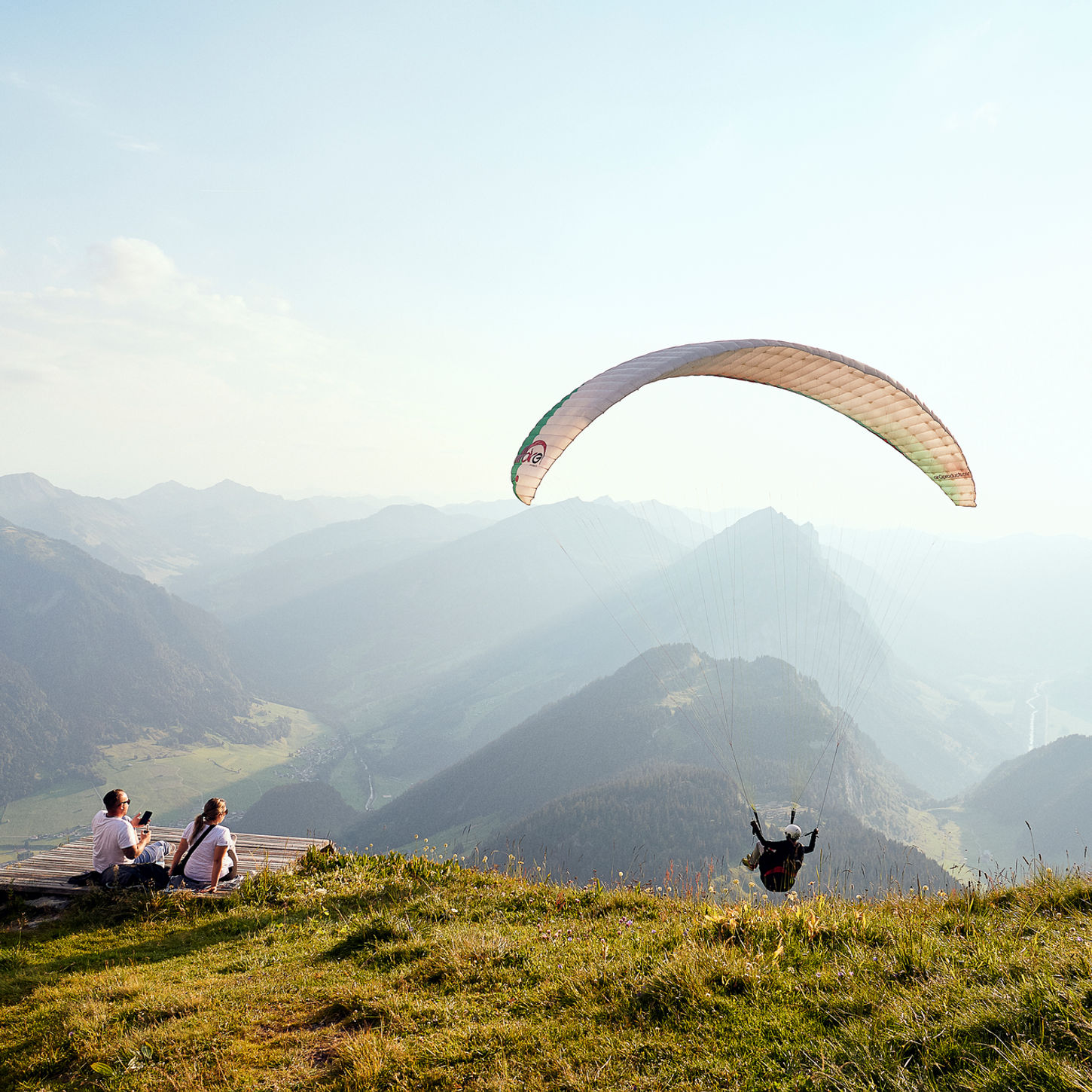 Paraglider fliegt über Berge mit Menschen, die auf dem Hügel sitzen und zusehen.