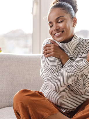 Woman practicing self-care at home while hugging herself and smiling, representing emotional wellness and self-love for the EveryHer Wellness blog post on common self-care myths and real self-care practices.