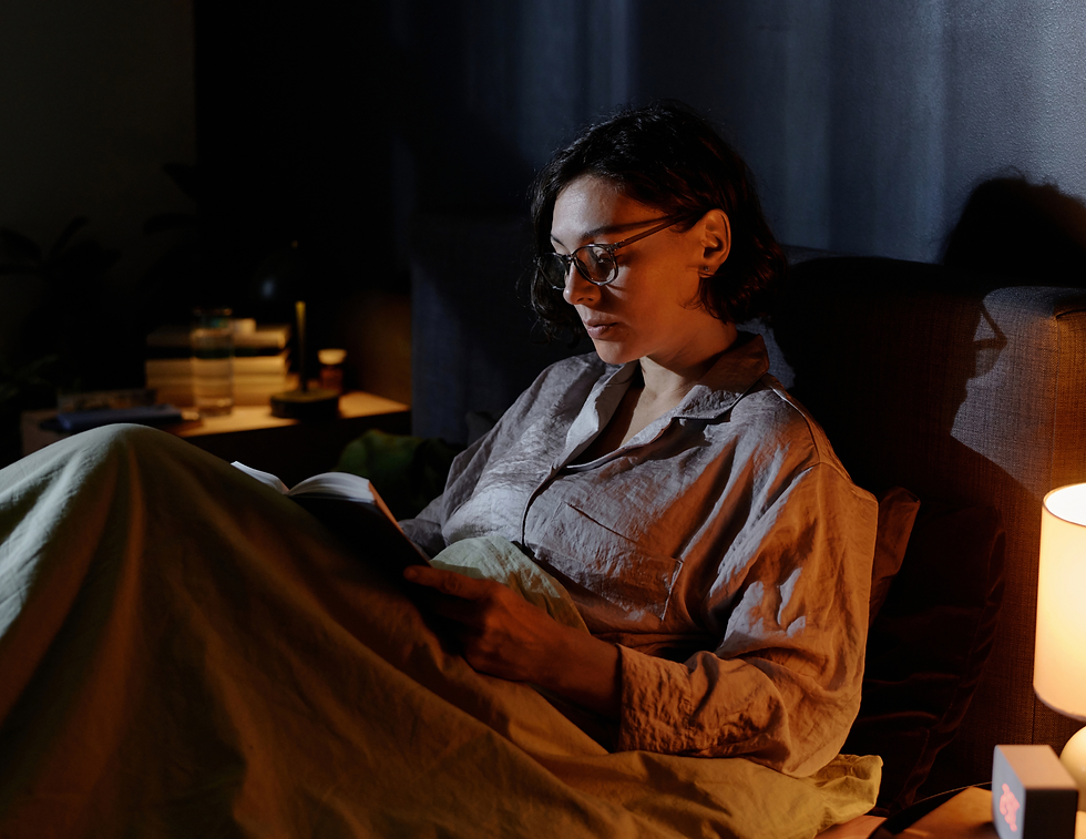 A woman winding down for the night, sitting in bed under a soft blanket, reading by warm lamp light as part of her evening self-care routine.