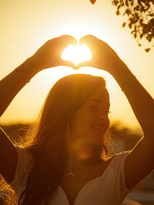 Woman smiling at sunset with hands forming a heart shape around the sun, symbolizing self-love, healing, and personal growth for EveryHer Wellness blog post “Becoming Unrecognizable, Growing into Who You’re Meant to Be