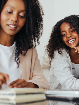 Single working mom smiling with her daughter while writing and using a laptop, practicing realistic time management for single working moms.
